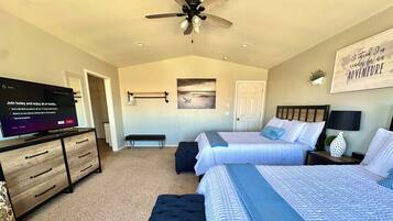 A bedroom with two beds, a TV, a ceiling fan, and a motivational wall art.