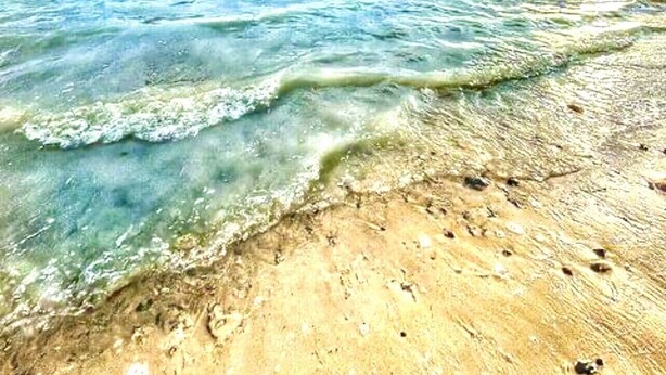 Une plage à l’eau turquoise et limpide, un rivage sablonneux et une formation rocheuse visible au loin.