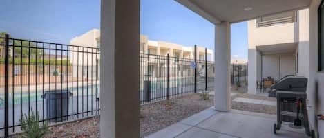A covered outdoor area with a barbecue grill, a pool, and a view of a building complex.