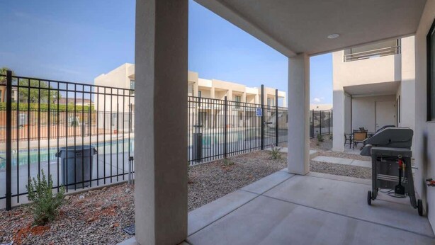 A covered outdoor area with a barbecue grill, a pool, and a view of a building complex.