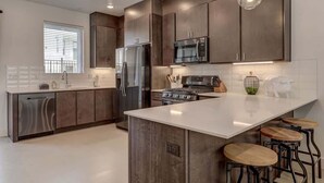 A modern kitchen with dark wood cabinets, stainless steel appliances, a central island with stools, and pendant lighting.