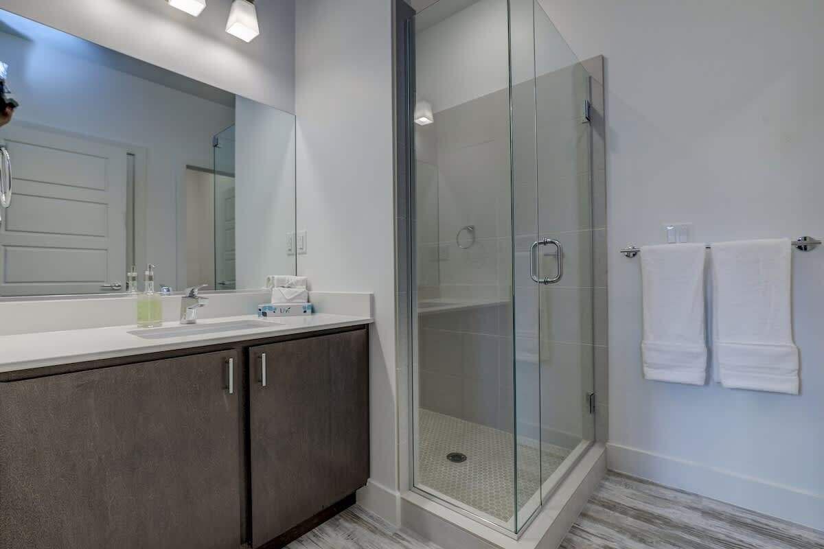 Une salle de bain moderne avec une douche à parois de verre, un grand miroir et un plan de toilette blanc.