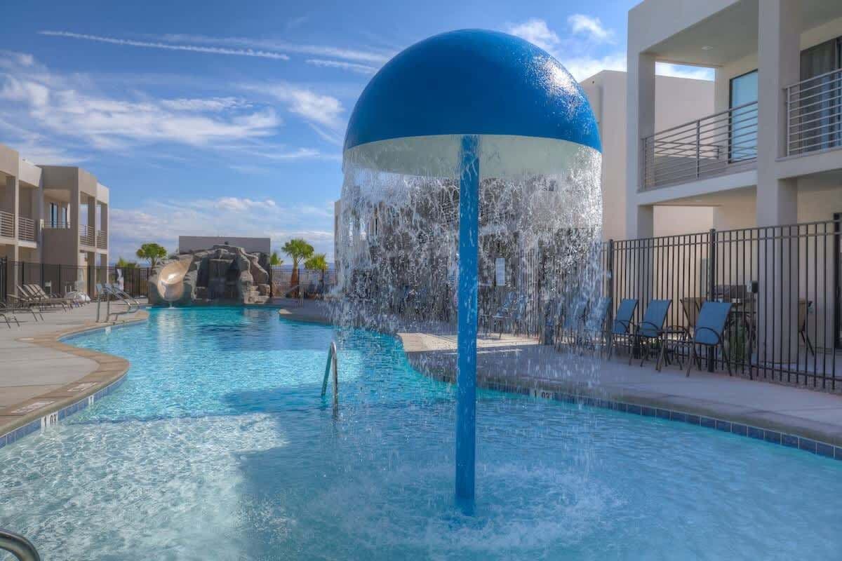 A swimming pool with a water feature, lounge chairs, and a building in the background.