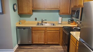 A kitchen with wooden cabinets, a stainless steel sink, a dishwasher, a microwave, and a refrigerator. - Affordable Rate with a Priceless View! (Sugar Mountain)