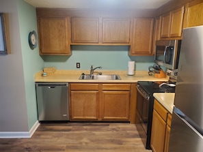 A kitchen with wooden cabinets, a stainless steel sink, a dishwasher, a microwave, and a refrigerator.