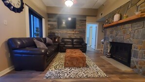 A living room with a stone fireplace, leather sofas, a coffee table, and a flat-screen TV mounted on the wall. - Affordable Rate with a Priceless View! (Sugar Mountain)