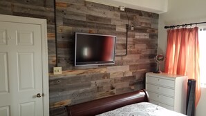 A bedroom with a wooden wall, a flat-screen TV, a bed, a dresser, and a window with curtains. - Affordable Rate with a Priceless View! (Sugar Mountain)
