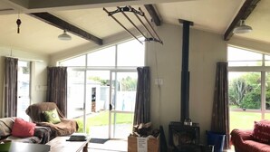 En rummelig stue med en stor pejs, en sofa, et sofabord og udsigt til det fri gennem store vinduer.