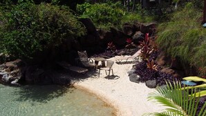 A clear pool with a sandy beach area, surrounded by rocks and lush greenery.