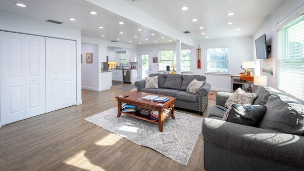 A spacious living room with a gray sofa, a wooden coffee table, and a kitchen in the background. - Casa la Cala - Serious Fun + Luxury Relaxation! (Safety Harbor)