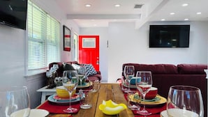 A dining area with a wooden table set for a meal, a red door in the background, and a red sofa. - Casa la Cala - Serious Fun + Luxury Relaxation! (Safety Harbor)