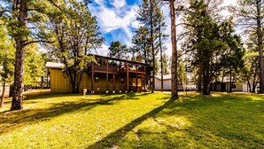 A two-story wooden cabin with a porch, surrounded by trees and a grassy yard. - The Gelk Pet Friendly | Live Large in the Pines—Hot Tub, Bar & Cozy Gathering Space (Alto)