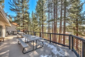 Une terrasse couverte avec des tables de pique-nique, un barbecue et une vue sur de grands pins.