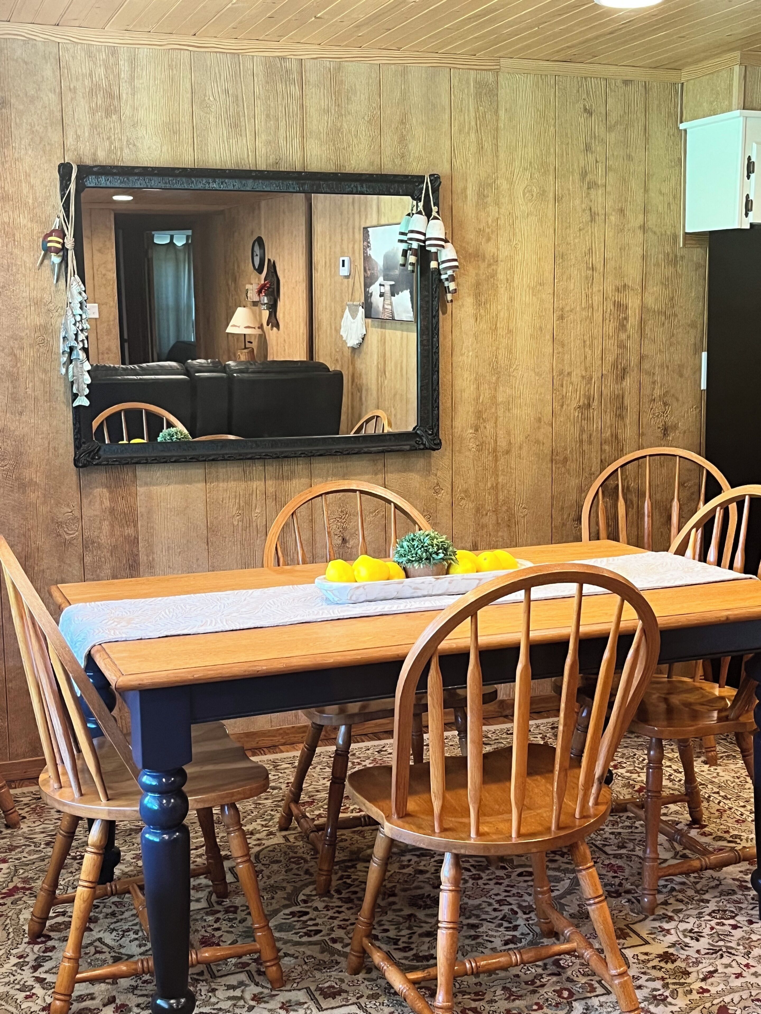 Un comedor con una mesa de madera, sillas, un espejo y una alfombra estampada.