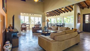 A spacious living room with a large beige sofa, a dining area with chairs, and a kitchen visible through an open door.