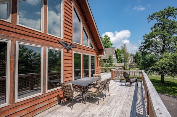 A wooden deck with a table and chairs, large windows, and a view of the surrounding area.