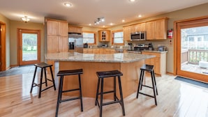 A spacious kitchen with wooden cabinets, a granite countertop, and a central island with stools. - Cozy Chalet w/ Views, Fireplaces & Fun (McHenry)