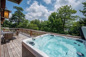 Ein Whirlpool auf einer Holzterrasse mit Blick auf Bäume und einen klaren Himmel.