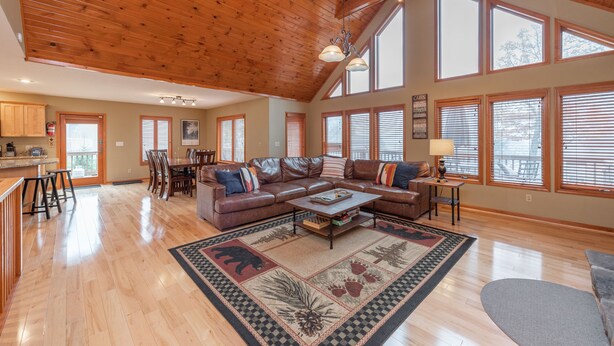 A spacious living room with a wooden ceiling, large windows, a leather sofa, and a coffee table. - Cozy Chalet w/ Views, Fireplaces & Fun (McHenry)