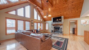 A spacious living room with a large brown leather sofa, a stone fireplace, and a wooden ceiling. - Cozy Chalet w/ Views, Fireplaces & Fun (McHenry)