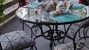 Eine Terrassengruppe im Freien mit einem Glastisch, gedeckt für das Essen, umgeben von Metallstühlen mit gemusterten Kissen.
