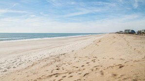 Een breed zandstrand met voetafdrukken die naar de oceaan leiden.
