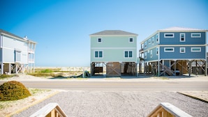 Een pand aan het strand met verhoogde houten constructies, een heldere lucht en een grindpad.