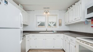 Een keuken met witte kastjes, een granieten aanrechtblad, een dubbele spoelbak en een magnetron.