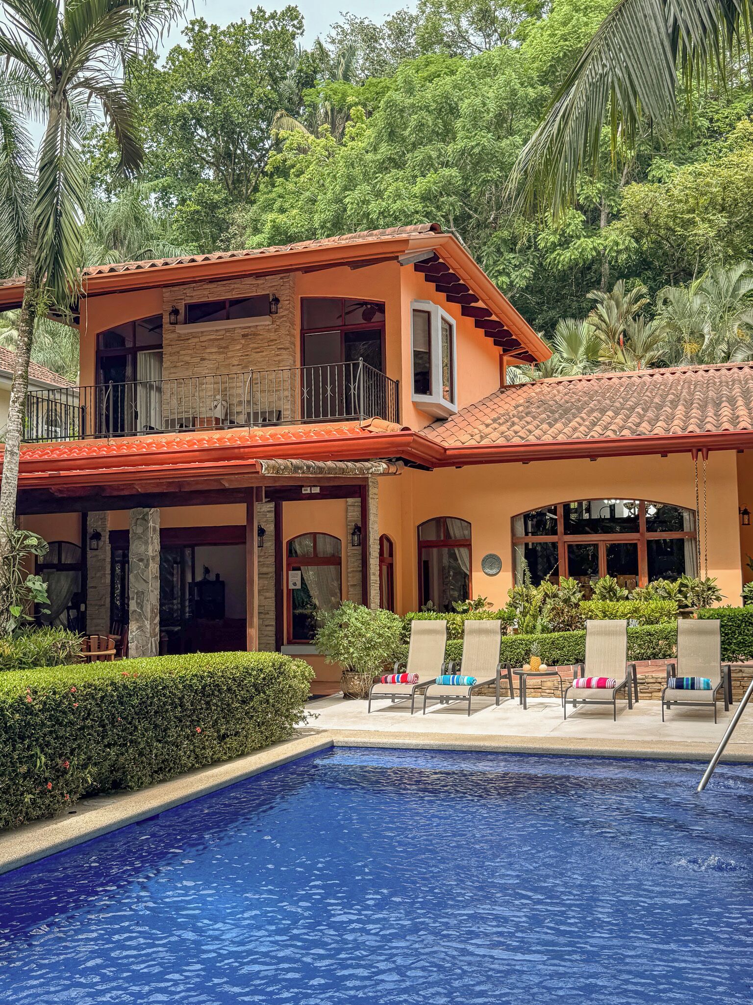A two-story house with a swimming pool, surrounded by lush greenery.