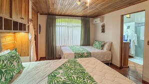 Une chambre avec deux lits, un plafond en bois, une salle de bain avec douche et une fenêtre avec des rideaux.