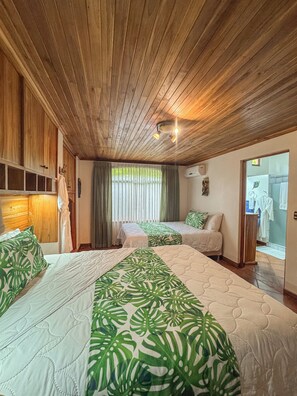 Ein Zimmer mit zwei Betten, Holzboden, einem Badezimmer mit Dusche und einem Fenster mit Vorhängen.