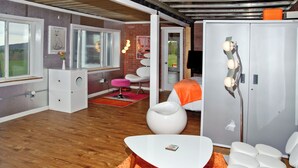A modern living room with a wooden floor, white furniture, a large white table, and a grey wardrobe with a light fixture. - Super Fun Shipping Container Home! Spacious and Stylish! (Sumner)