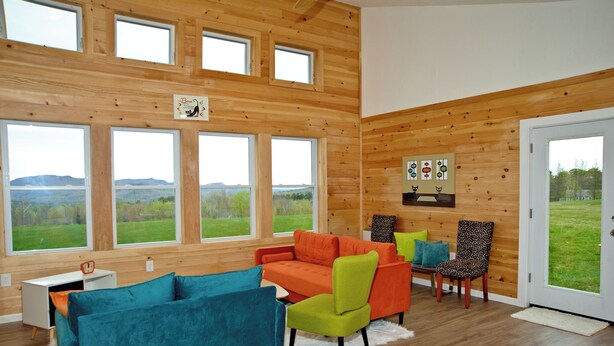 A room with large windows, wooden walls, a sofa, chairs, and a desk. - Super Fun Shipping Container Home! Spacious and Stylish! (Sumner)