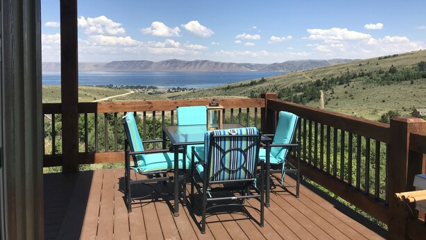 Een houten terras met twee stoelen en een tafel, met uitzicht op een schilderachtig landschap met bergen en water.