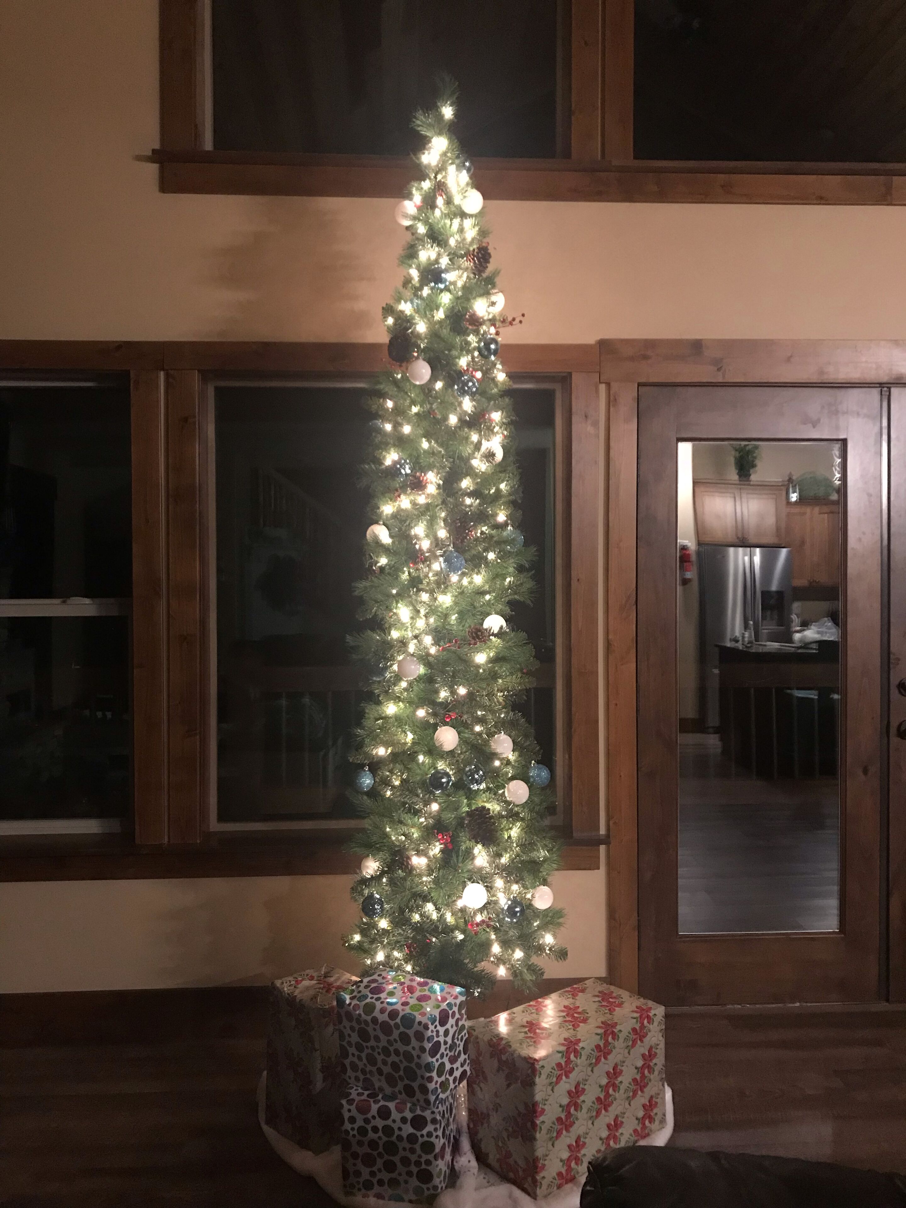 Ein Weihnachtsbaum mit Lichtern und Schmuck in einem Zimmer mit Holzböden und großen Fenstern.