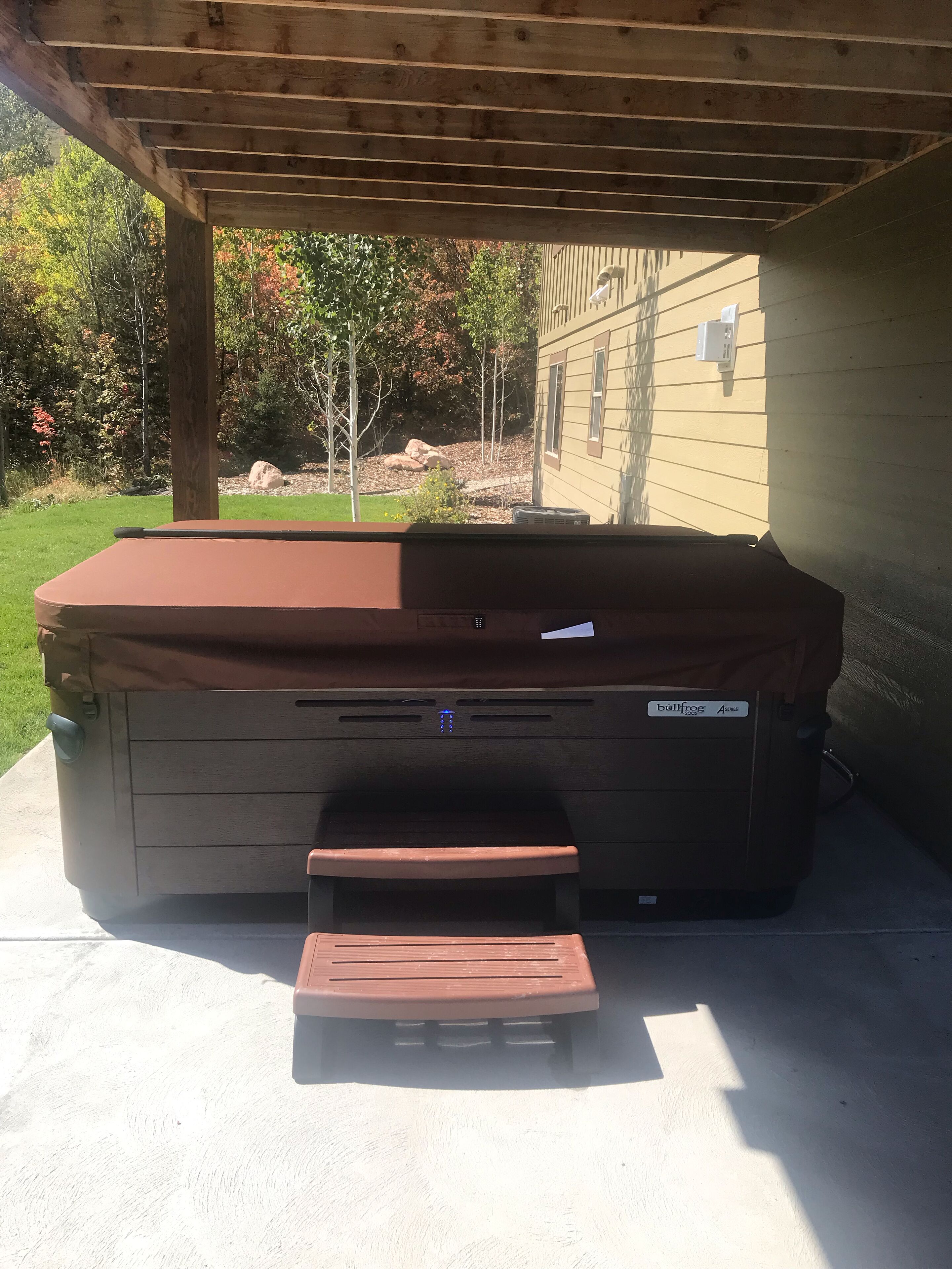 Un jacuzzi bajo una pérgola de madera con un banco en frente.