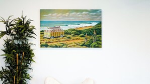 Ein Zimmer mit einem weißen Stuhl, einer Topfpflanze, einer Korbsitzbank und einem Bild von einer Strandlandschaft.