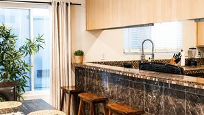Eine moderne Küche mit Holzschränken, einer Marmor-Spritzschutzwand und einem Essbereich mit Tisch und Hockern.