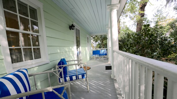 A porch with a white railing, a wicker chair with blue cushions, and a blue and white striped pillow. - QUAINT COTTAGE IN HISTORIC OLD POINT   Beaufort, S.C. (Beaufort)