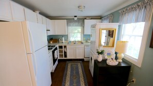 A compact kitchen with white cabinets, a central island, a sink, and a stove. - QUAINT COTTAGE IN HISTORIC OLD POINT   Beaufort, S.C. (Beaufort)