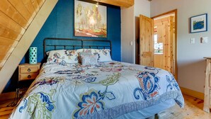 A bedroom with a sloped ceiling, a bed with a floral-patterned bedspread, a wooden nightstand, and a painting on the wall. - Mountain Views, Hot Tub, Incredible Location! Dog Friendly! 
BCA-47331 (Dillon)