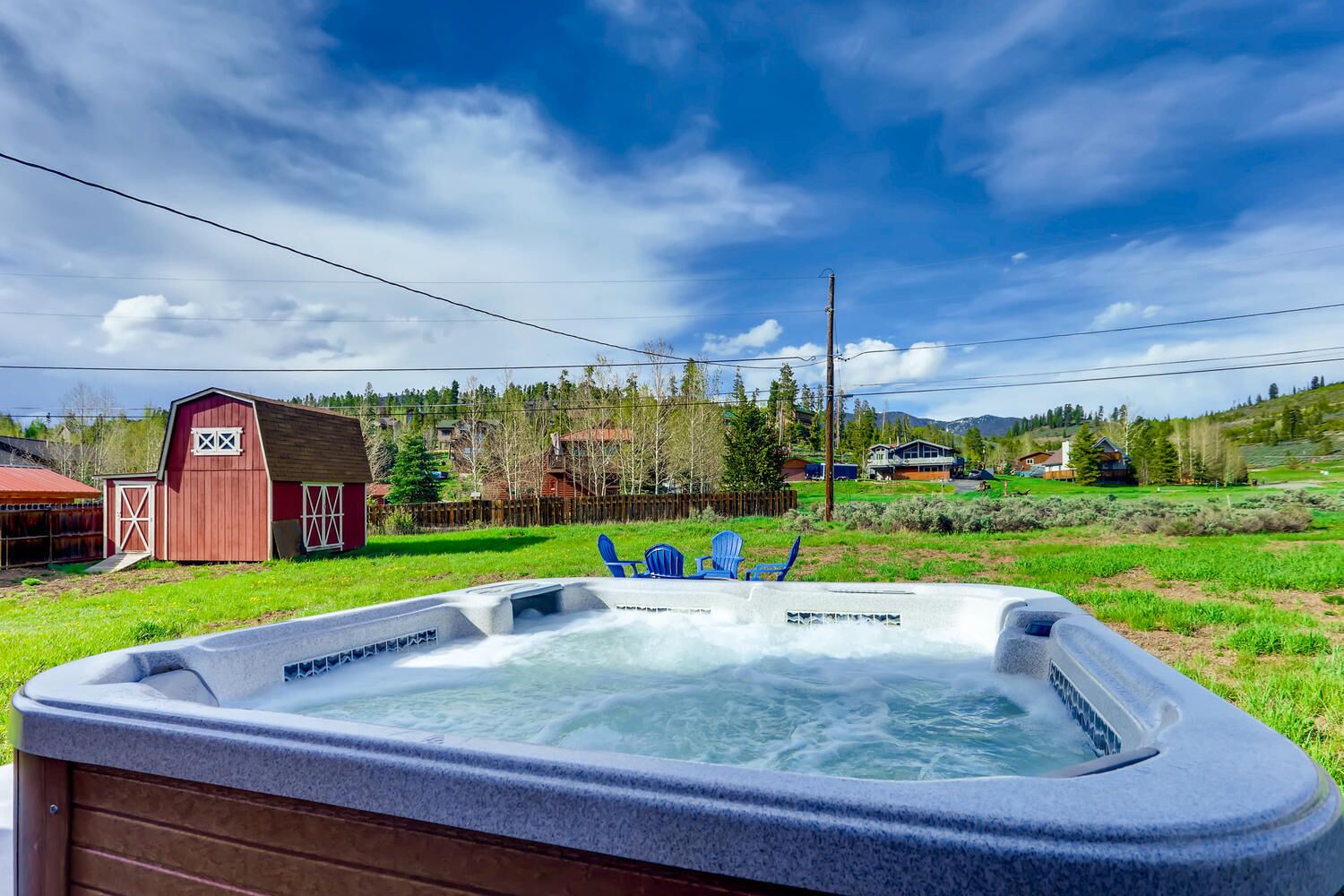 A hot tub in a backyard with a red barn and a wooden fence.