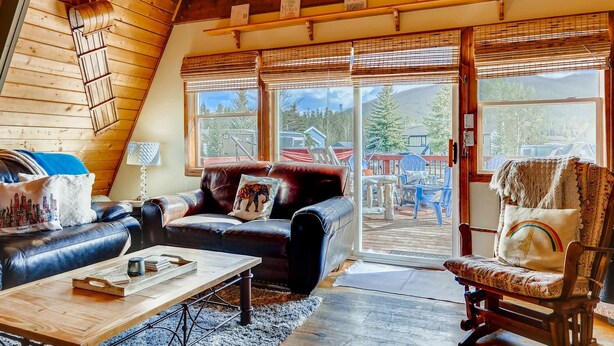 A cozy living room with a leather sofa, a wooden coffee table, and a view of the outdoors through large sliding glass doors. - Mountain Views, Hot Tub, Incredible Location! Dog Friendly! 
BCA-47331 (Dillon)