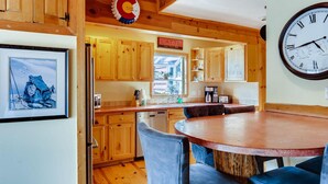 A kitchen with wooden cabinets, a dining table with chairs, a clock, and a framed picture on the wall. - Mountain Views, Hot Tub, Incredible Location! Dog Friendly! 
BCA-47331 (Dillon)