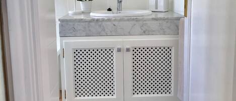 Un baño con tocador blanco, lavabo, espejo, toallero y una pequeña orquídea en maceta.