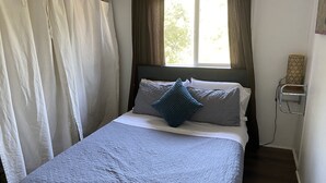 Ein ordentlich bezogenes Bett mit einer blauen Steude, weißen Kissen und einem grauen Kopfteil.