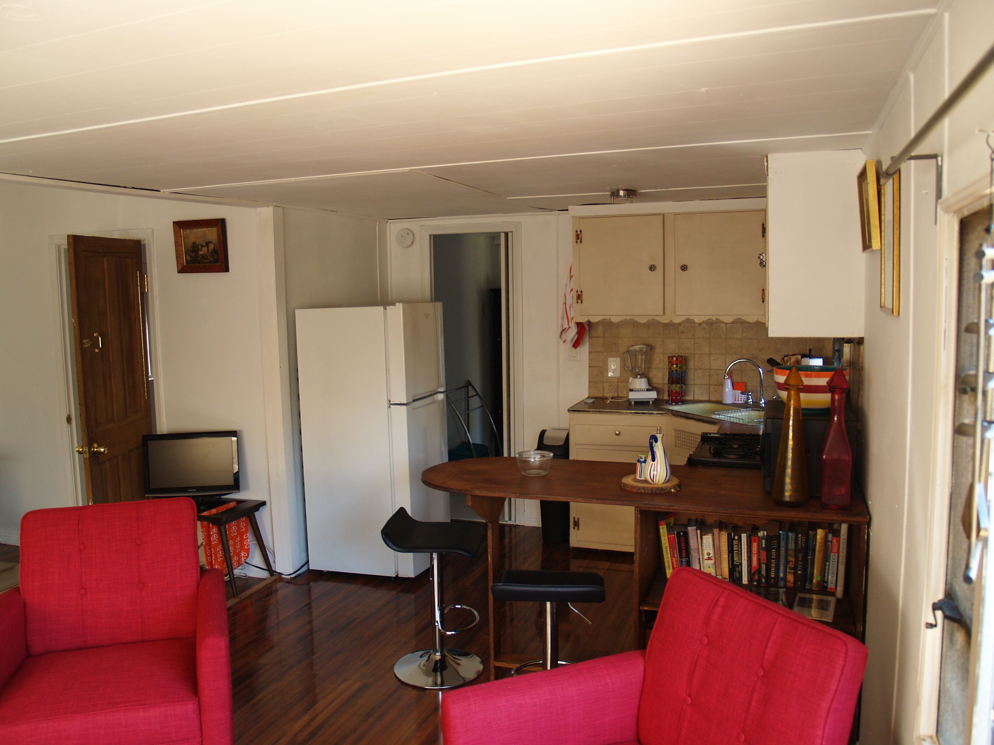 Un espacio habitable compacto con kitchenette, una zona de comedor con un taburete de bar y dos sillones rojos.