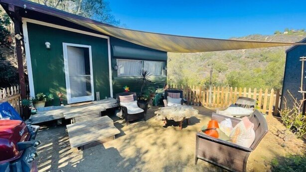 Eine überdachte Terrasse im Freien mit Sitzgelegenheit, einem kleinen Tisch und einem Grill.