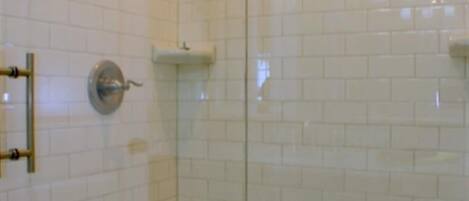 Eine gläserne Dusche mit weißen Fliesen im U-Bahn-Stil und einem goldfarbenen Duschkopf.