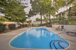 A swimming pool with a green fence, lounge chairs, and a building in the background. - Cozy Cottage in Downtown Branson with a Pool  (Branson)